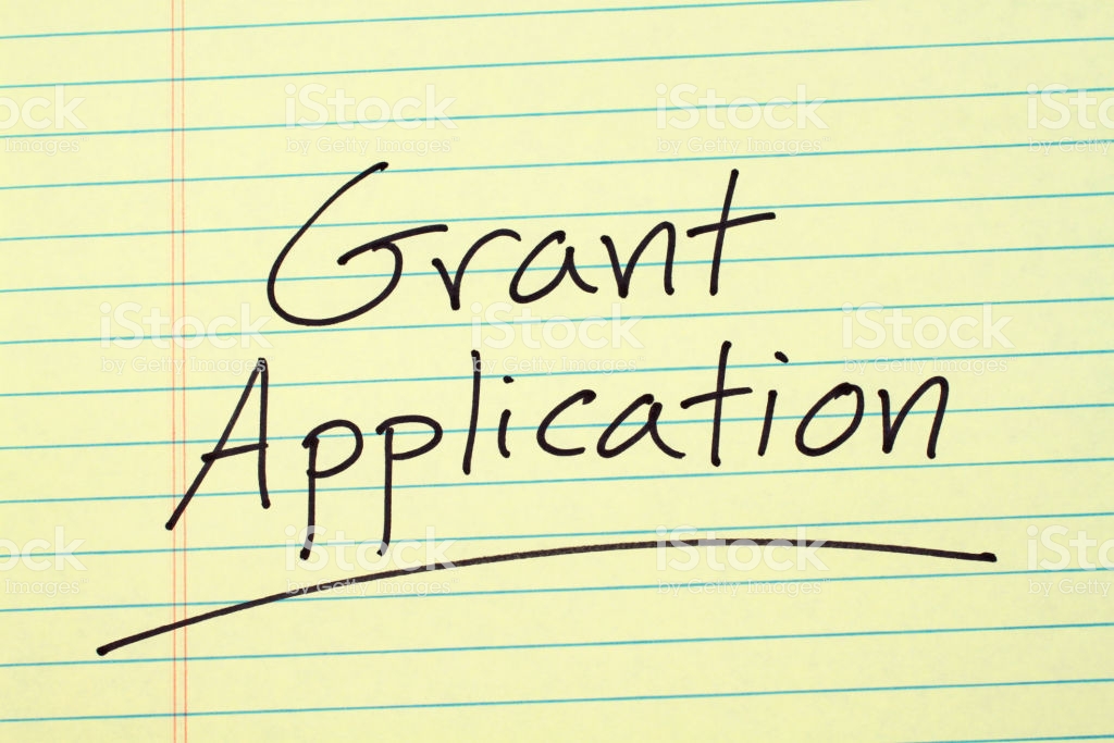 The word “Grant Application” underlined on a yellow legal pad